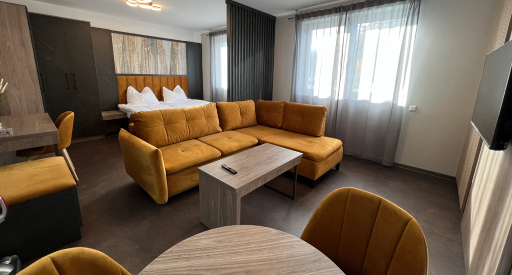 Gemütliches und modernes Lounge-Areal einer Pension mit einer gelben Eckcouch, runden Sesseln und Holztischen, repräsentativ für die qualitätsvolle Einrichtung von Pensionen.