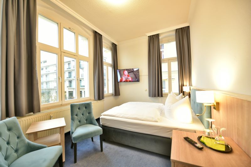 Helles Hotelzimmer mit polnischen Hotelmöbeln, ausgestattet mit einem komfortablen Doppelbett, einem eleganten türkisen Sessel, einem Holzschreibtisch und modernen Annehmlichkeiten wie einem Flachbildfernseher.